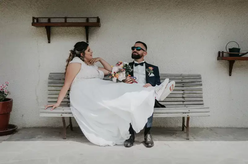 Les mariés sont assis sur un banc pour une photo originale et drôle
